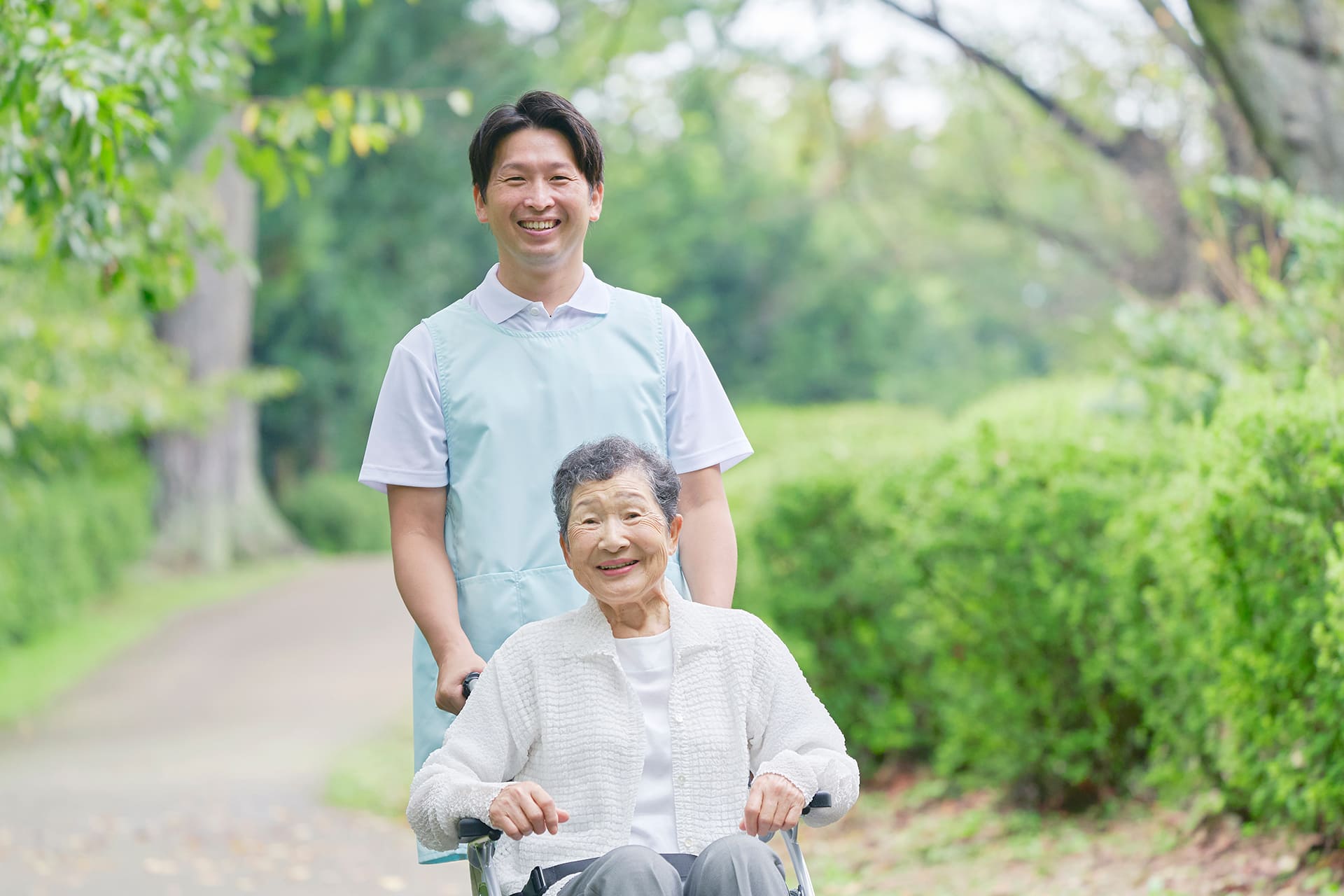介護士と車いすに乗った女性が笑顔で散歩に出かけている様子